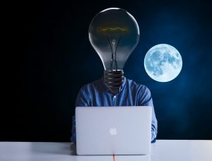 un homme devant un ordinateur avec une ampoule à la place de la tête, la lune en arrière plan